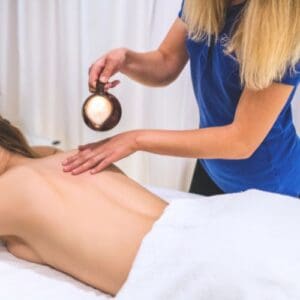 Terapeutka spa rozprowadza olejek ze świecy aromaterapeutycznej na plecach klientki